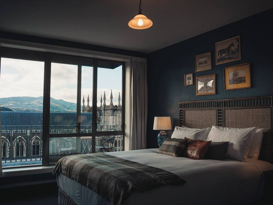 A bedroom with a large window, a bed with pillows, and a headboard with framed pictures.