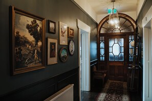 Een gang met ingelijste kunstwerken, een radiator, en een houten deur met glas-in-lood.
