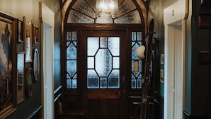 Un couloir avec un tapis à motifs, une porte en bois dotée de panneaux de verre et un lustre.