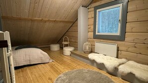 Een gezellige slaapkamer op zolder met een schuine wand, een groot raam met zonwering, een bed met een gewatteerde deken, een zachte witte plaid en een rond vloerkleed.