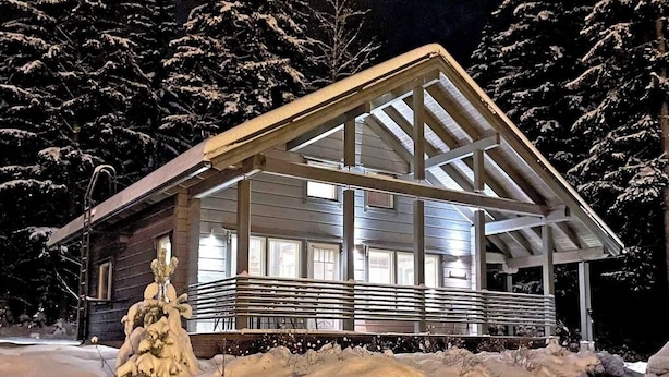 Een houten hut met een overdekte veranda en grote ramen, omgeven door met sneeuw bedekte bomen.