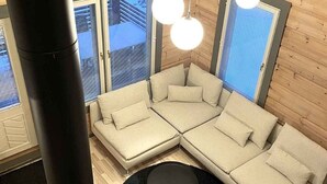 Een moderne woonkamer met een hoekbank, een ronde zwarte salontafel en een groot raam met zonwering.
