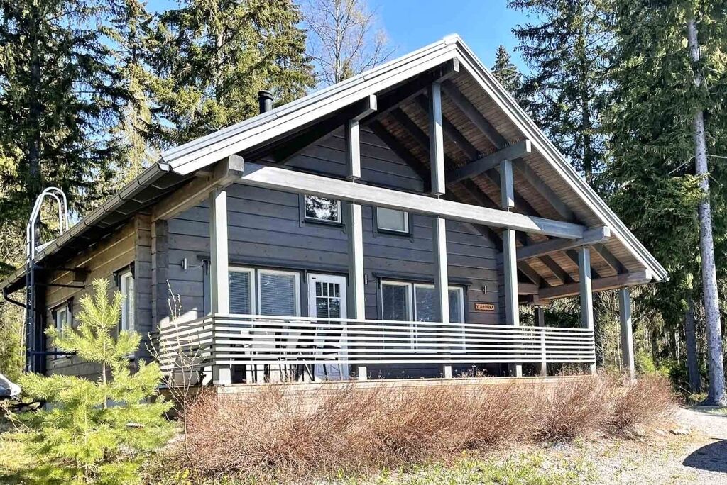 Eine zweistöckige Holzhütte mit überdachter Veranda, umgeben von Bäumen.
