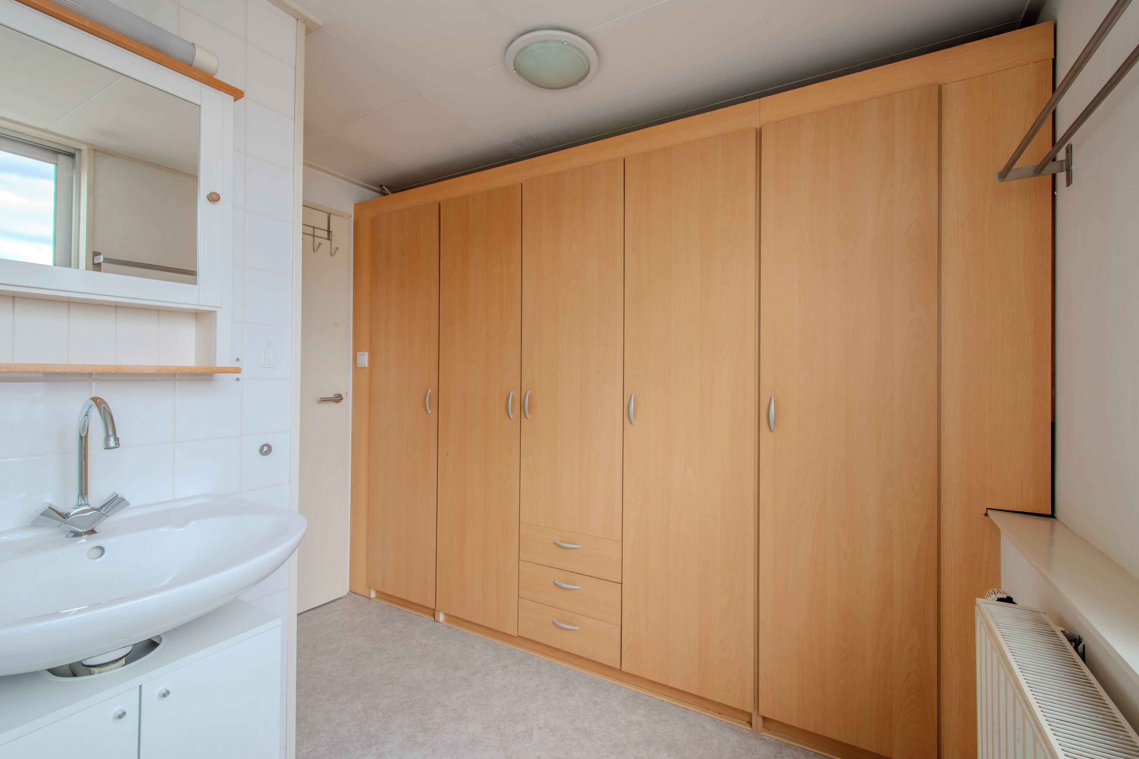 Een badkamer met een wit wastafelmeubel, spiegel en een houten garderobe met lades.