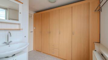 Een badkamer met een wit wastafelmeubel, spiegel en een houten garderobe met lades.