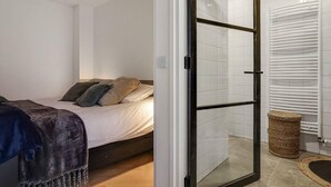 Ein Schlafzimmer mit einem Bett, einer Glastür zu einem Badezimmer und einer weißen Fliesenwand.