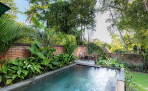 A rectangular pool with a brick wall and lush greenery surrounding it. - Tegal Harum Villas (Ubud)