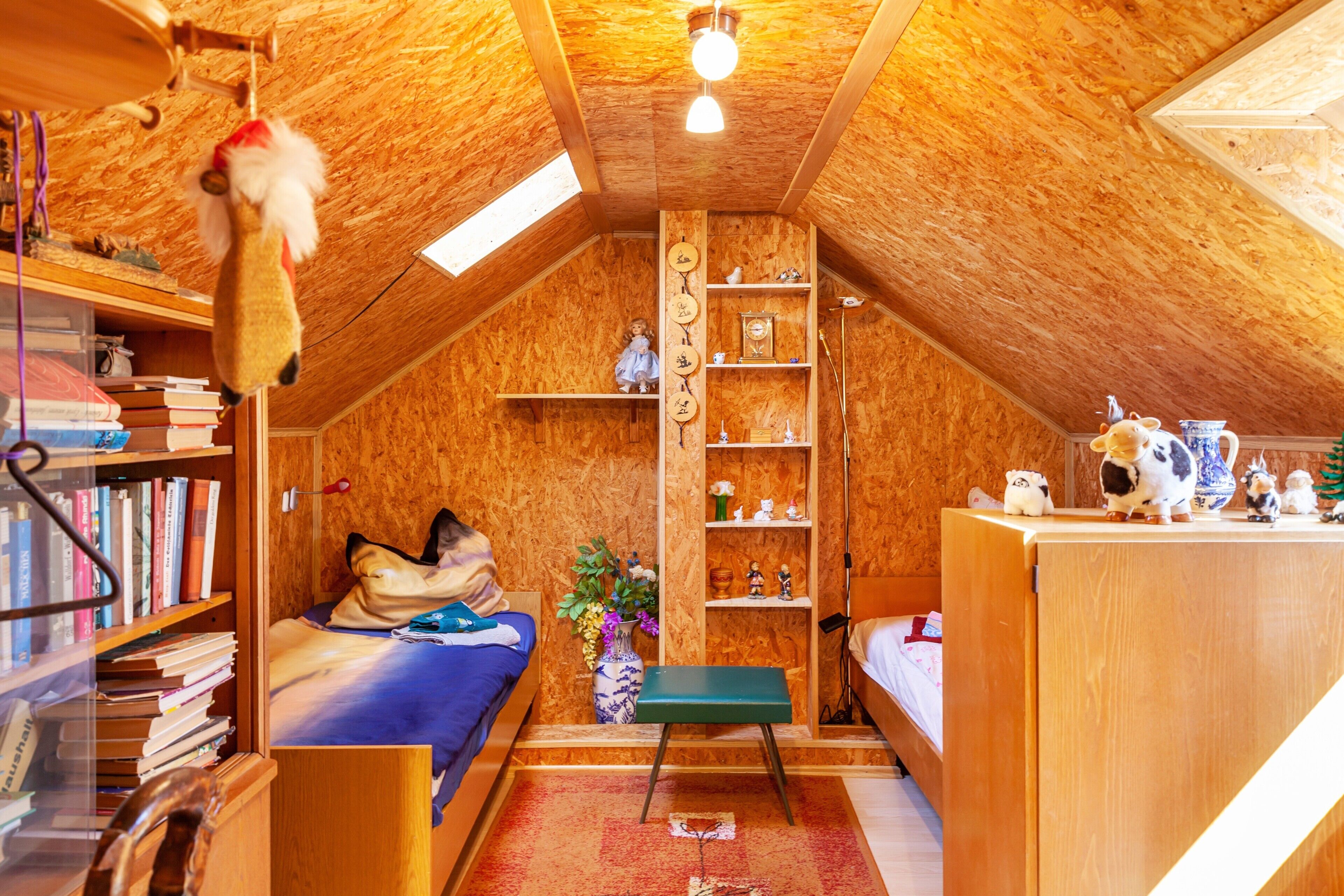 A cozy attic bedroom with wooden walls, a bunk bed, a desk, and a bookshelf.