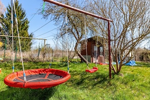Een trampoline met schommels, een houten constructie en een boom in een grasveld.