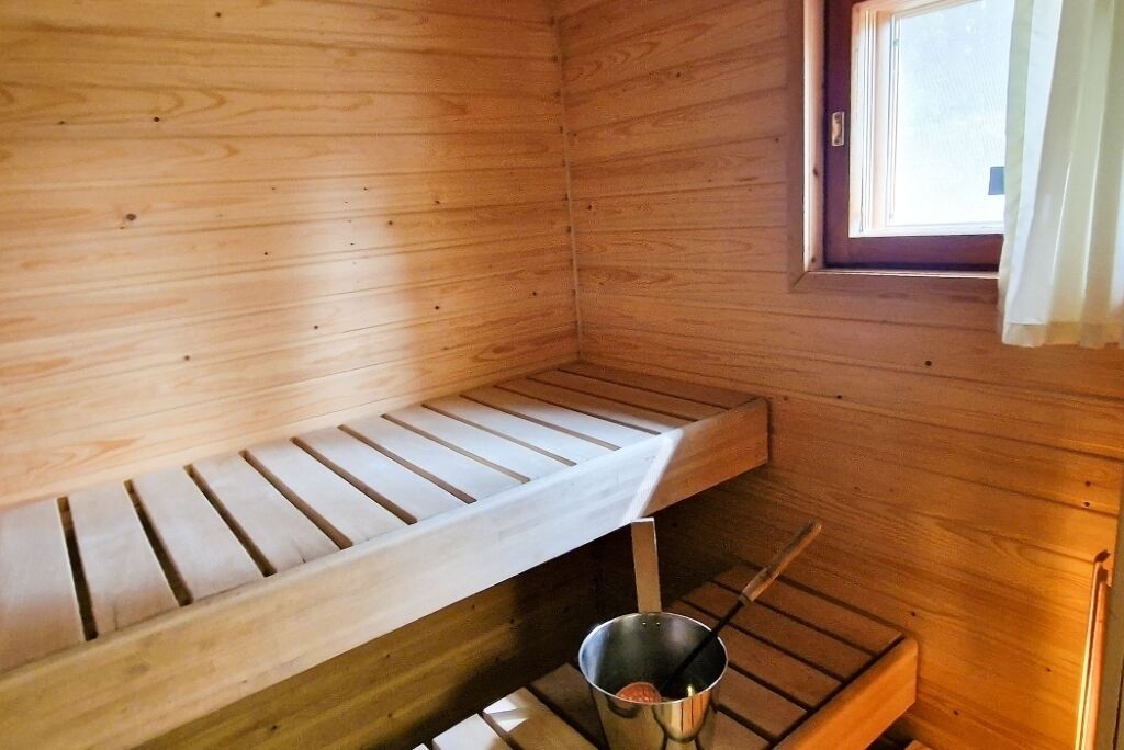 Een houten sauna met een bank, een emmertje en een raam met gordijnen.