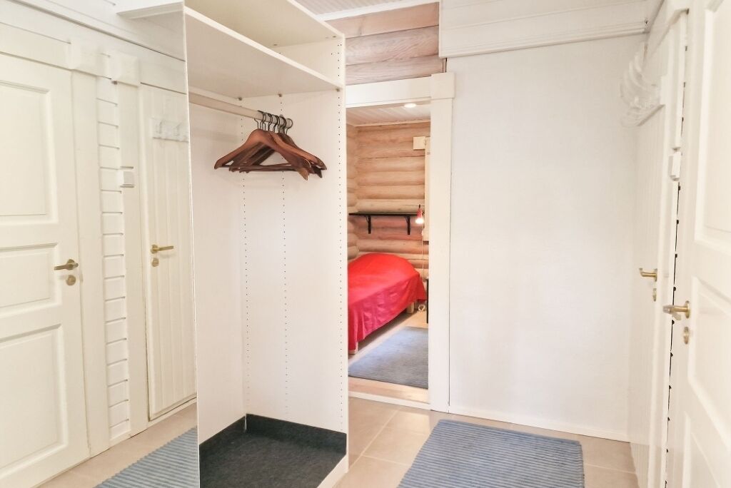 Un armari amb porta i un penjador de fusta, amb un llit a la sala adjacent.