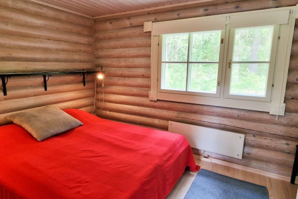 Quarto de cabana de madeira com cama, janela e luminária fixada na parede.