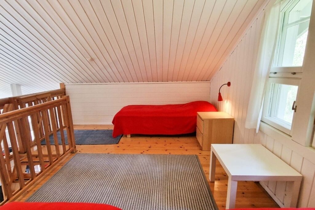 Una habitación pequeña y acogedora con techo inclinado, una cama de madera, una mesita de noche, un escritorio pequeño y una ventana.