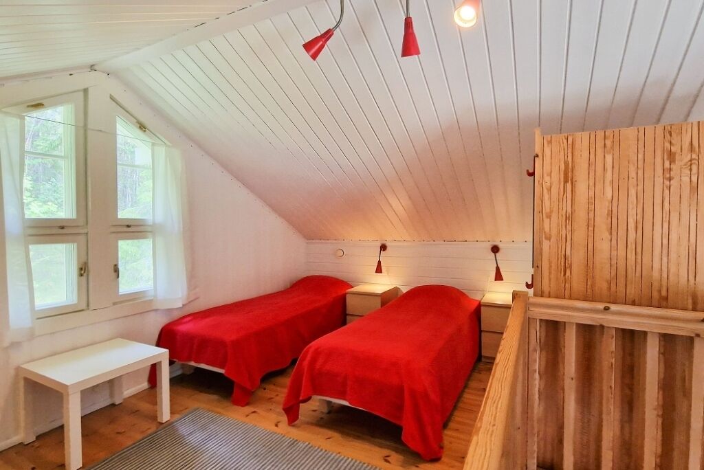 A small, cozy room with two single beds, a wooden bench, and a window with curtains.