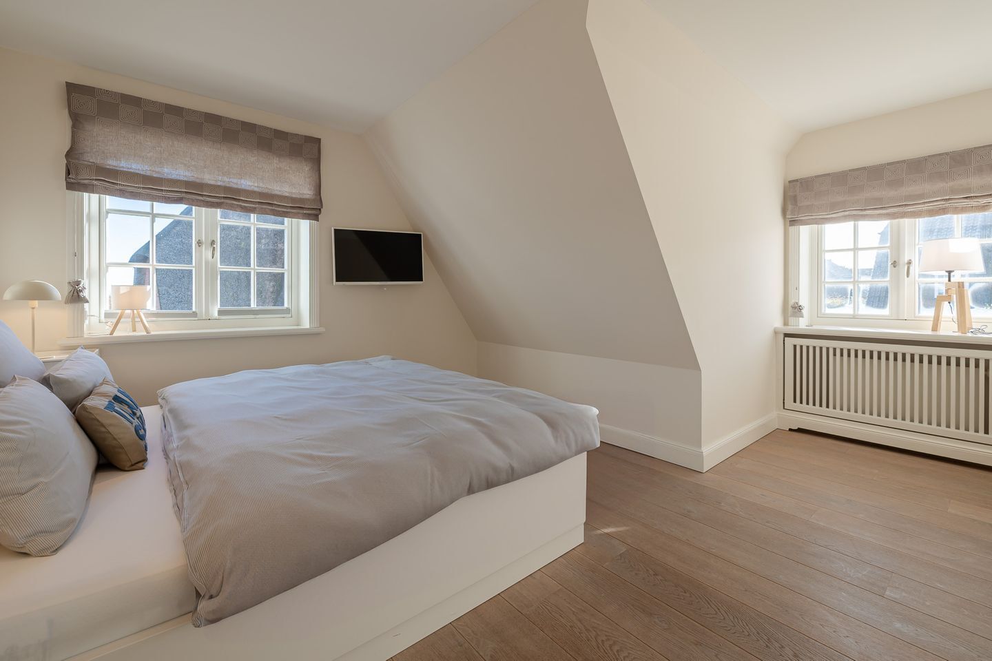 Une chambre à coucher avec un lit, une télévision, un radiateur et des fenêtres avec des rideaux.