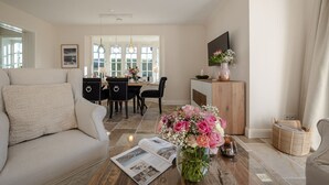 A living room with a sofa, a dining table with chairs, a coffee table with a magazine, and a vase of flowers. - Finn's Hüs - A Stylish Thatched-Roof House in Wenningstedt on Sylt (Wenningstedt-Braderup (Sylt))