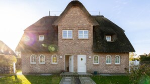 A two-story brick house with a steeply pitched roof, a central entrance with a white door, and multiple windows. - Finn's Hüs - A Stylish Thatched-Roof House in Wenningstedt on Sylt (Wenningstedt-Braderup (Sylt))