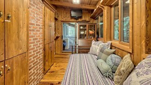 L’intérieur d’un chalet en bois présente un coin salon accueillant, un mur en briques et un téléviseur fixé au plafond.
