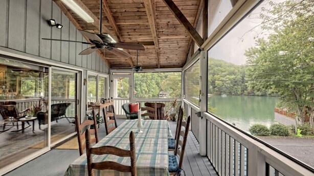 A covered outdoor deck with a table and chairs, overlooking a lake.