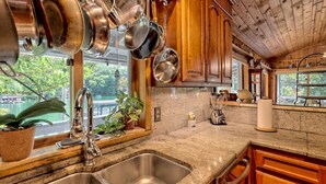 A kitchen with granite countertops, stainless steel sink, wooden cabinets, and hanging pots.