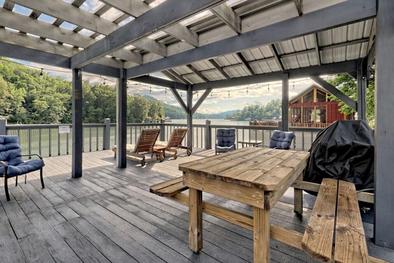 A covered deck with wooden furniture, a table, and a grill.