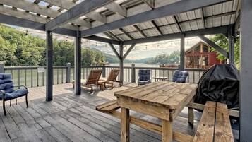 A covered deck with wooden furniture, a table, and a grill.
