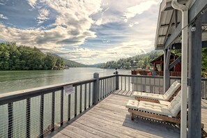 En træterrasse med gelænder og udsigt over en sø, med en liggestol og et overdækket siddeområde.