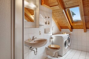 A bathroom with a sink, toilet, and washing machine, wooden beams, and a skylight. - Apartment Cheny with Hochschwarzwald Card (Titisee-Neustadt)