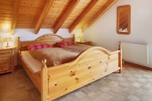 A wooden bed in a room with a sloped ceiling, a bedside table, a lamp, and a radiator. - Apartment Cheny with Hochschwarzwald Card (Titisee-Neustadt)