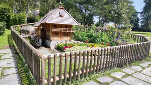 A wooden cabin with a sloped roof, surrounded by a wooden fence and a garden with various flowers. - Apartment Cheny with Hochschwarzwald Card (Titisee-Neustadt)