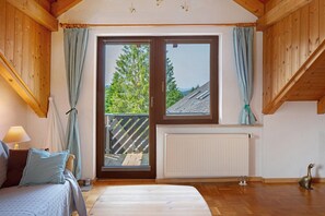 Une pièce avec un lit, une fenêtre avec des rideaux, un radiateur et un plancher en bois.