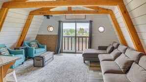 Ein gemütliches Schlafzimmer im Dachgeschoss mit schrägen Wänden, Holzbalken, einer großen Schiebeglastür zu einem Balkon und Blick ins Freie.
