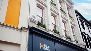 Un bâtiment à la façade blanche, doté d’une marquise noire et d’un logo sur lequel on peut lire « higgi haus ».