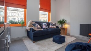Un salon moderne avec un canapé bleu foncé, des stores orange, une plante en pot et un radiateur.