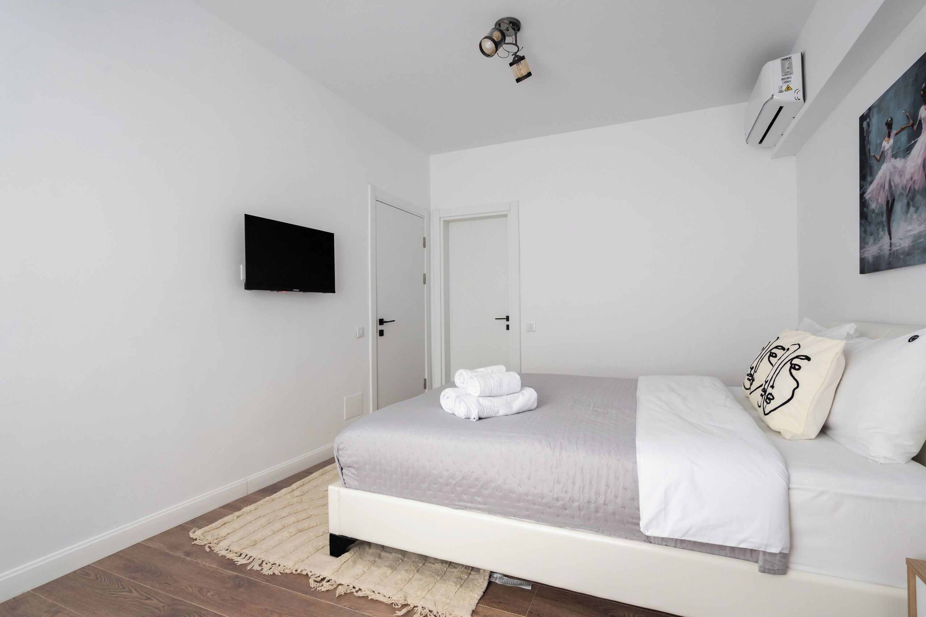 A bedroom with a bed, a flat-screen TV, an air conditioner, and a painting on the wall.