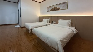 A hotel room with two beds, wooden flooring, a painting on the wall, and a door to the left. - PALA Garden Hotel (Vientiane)