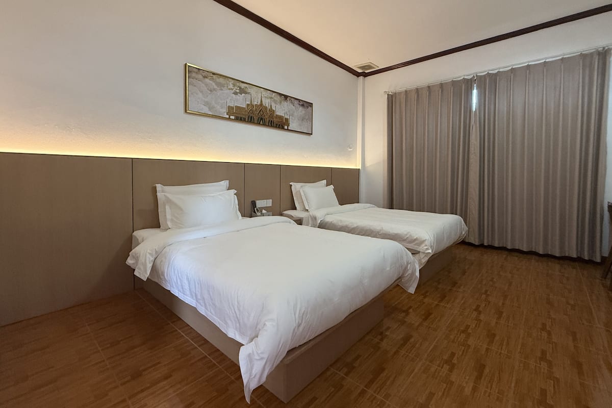 Habitación de hotel con dos camas, un ventanal con cortinas y un cuadro en la pared.