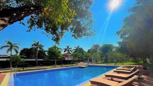 A swimming pool with lounge chairs and a wooden deck, surrounded by trees and buildings. - PALA Garden Hotel (Vientiane)
