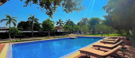 A swimming pool with lounge chairs and a wooden deck, surrounded by trees and buildings.