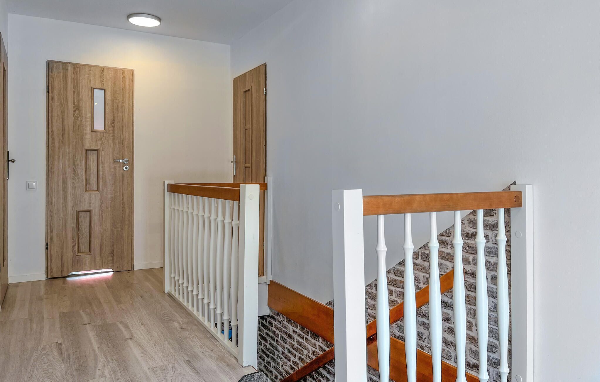 Un couloir avec des portes en bois, une rambarde blanche et un escalier doté d’une main courante en bois.