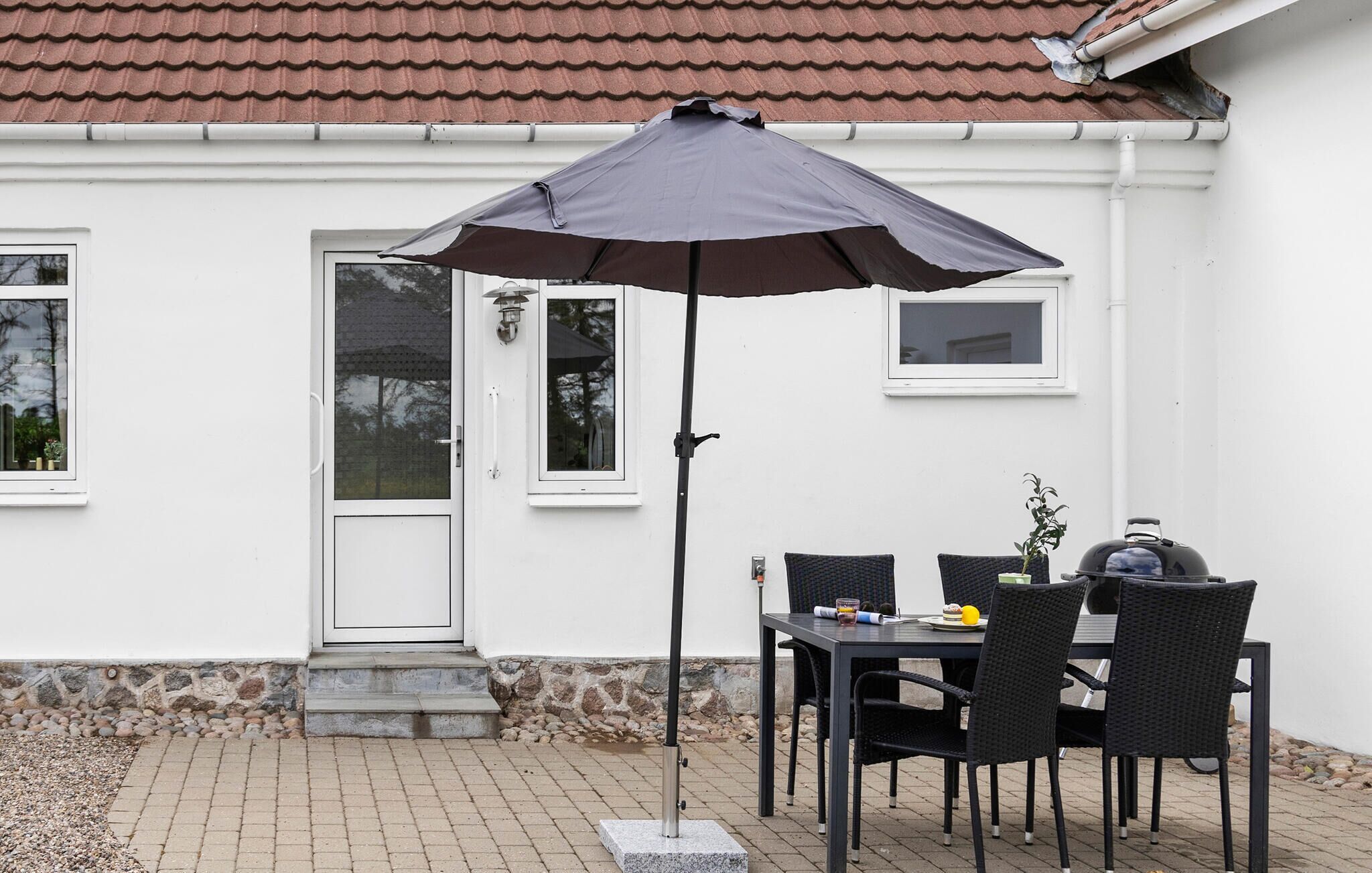 En udendørs terrasse med et bord, stole, grill og stor parasol.