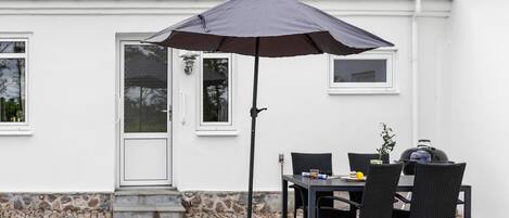En udendørs terrasse med et bord, stole, grill og stor parasol.