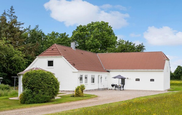 Une maison blanche avec un toit brun, une allée en gravier et une petite terrasse avec une table et des chaises.
