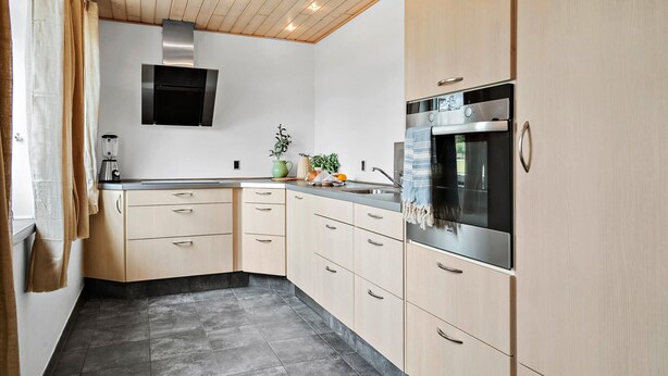 A modern kitchen with light wood cabinets, a built-in oven, and a black stove.
