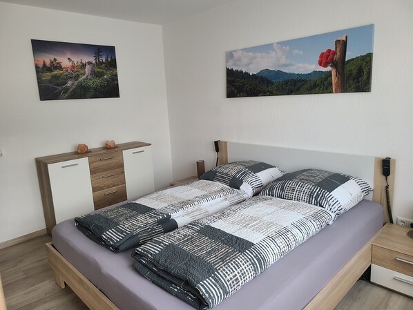 Un lit bien fait, avec une literie à motifs, une tête de lit en bois, une table de chevet avec une lampe et deux tableaux accrochés au mur.