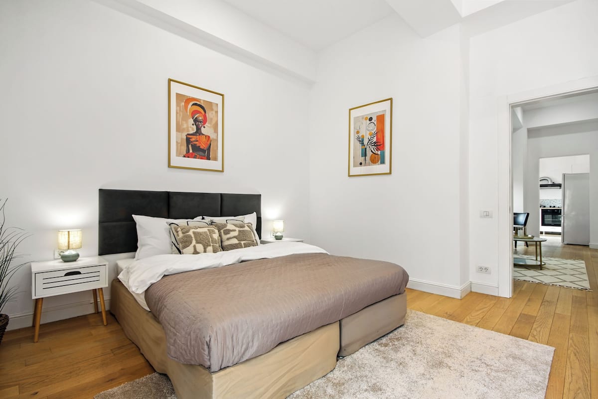 A modern bedroom with a bed, bedside tables, and artwork on the walls.