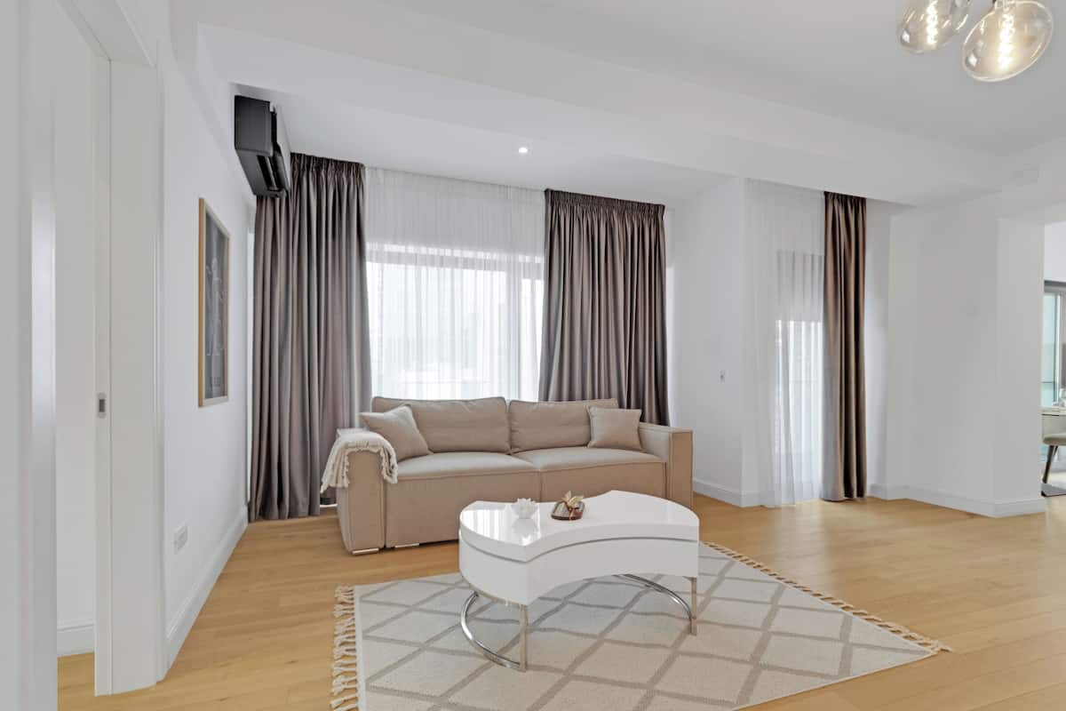 A modern living room with a beige sofa, a white coffee table, and a patterned rug.