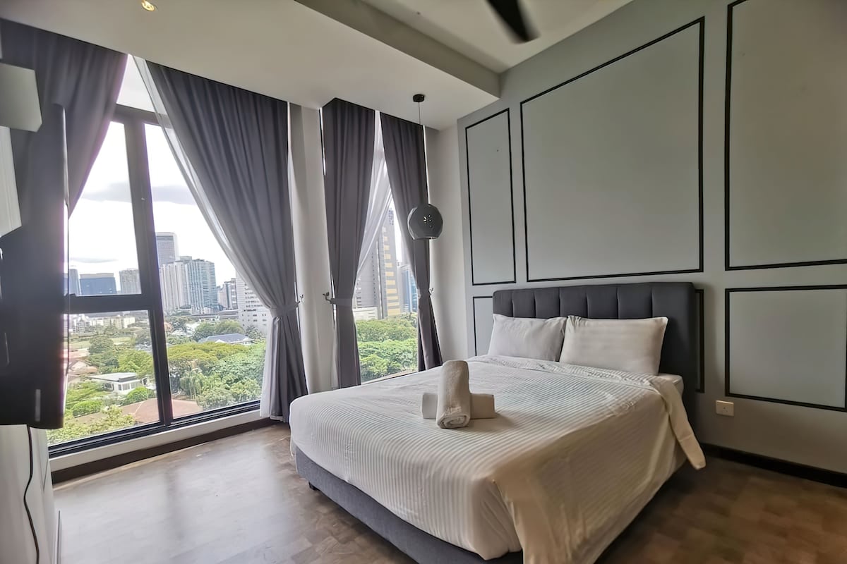 Quarto de hotel moderno com uma cama grande, vista para a cidade e uma ampla janela com cortinas.