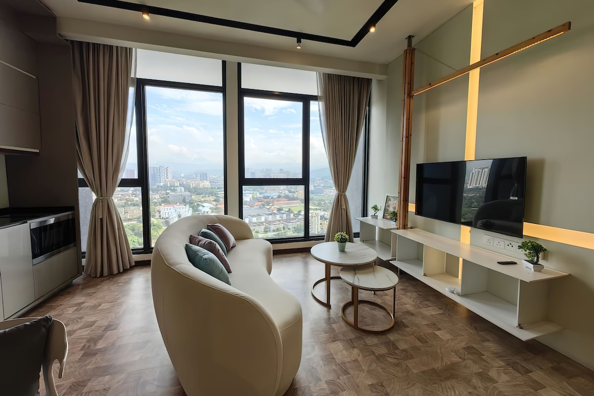Uma sala de estar moderna, com um sofá, uma televisão e vista para a cidade através de grandes janelas.