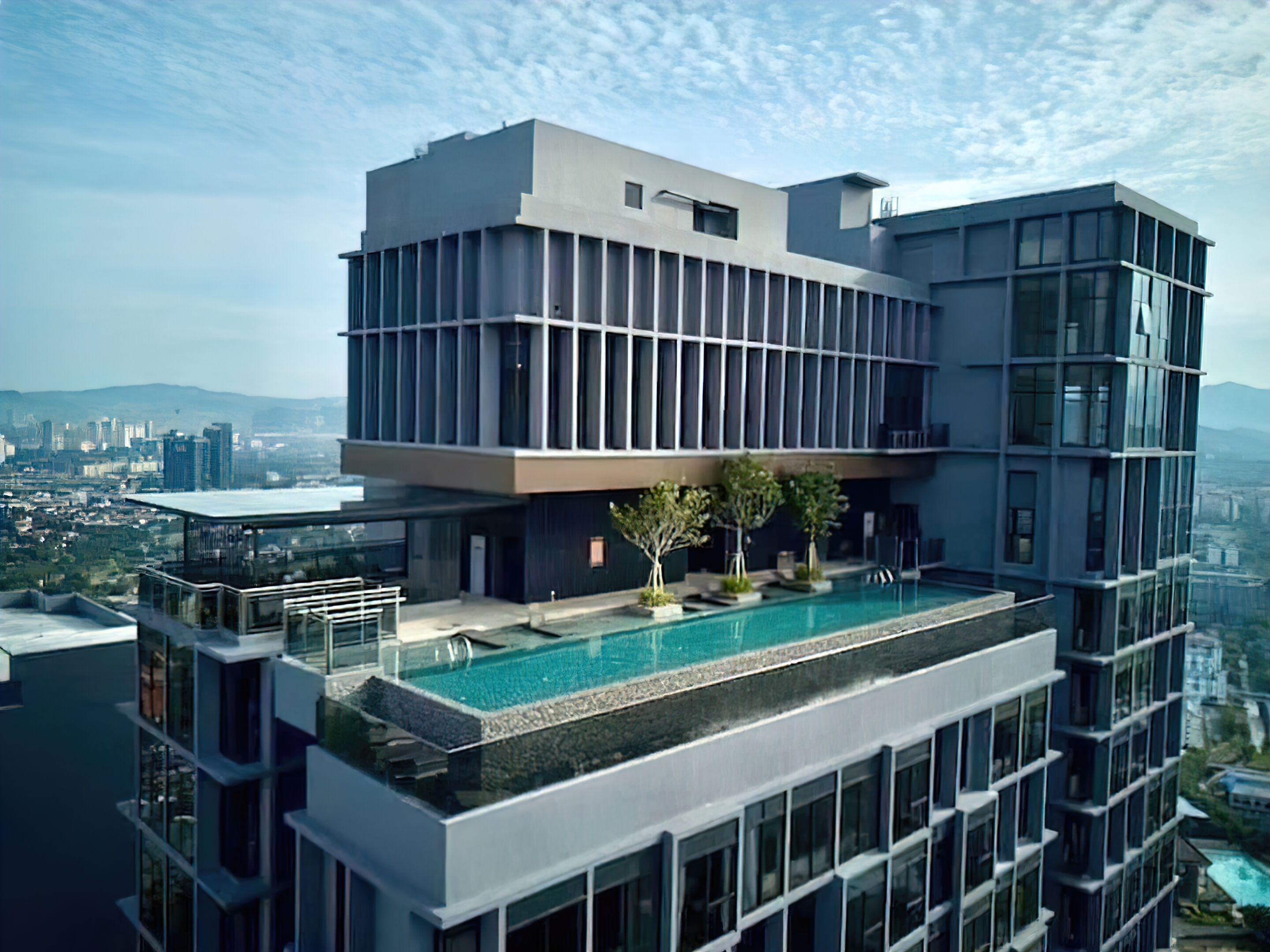 Un edificio moderno de gran altura con piscina en la azotea, amplias ventanas y vistas panorámicas de la ciudad.